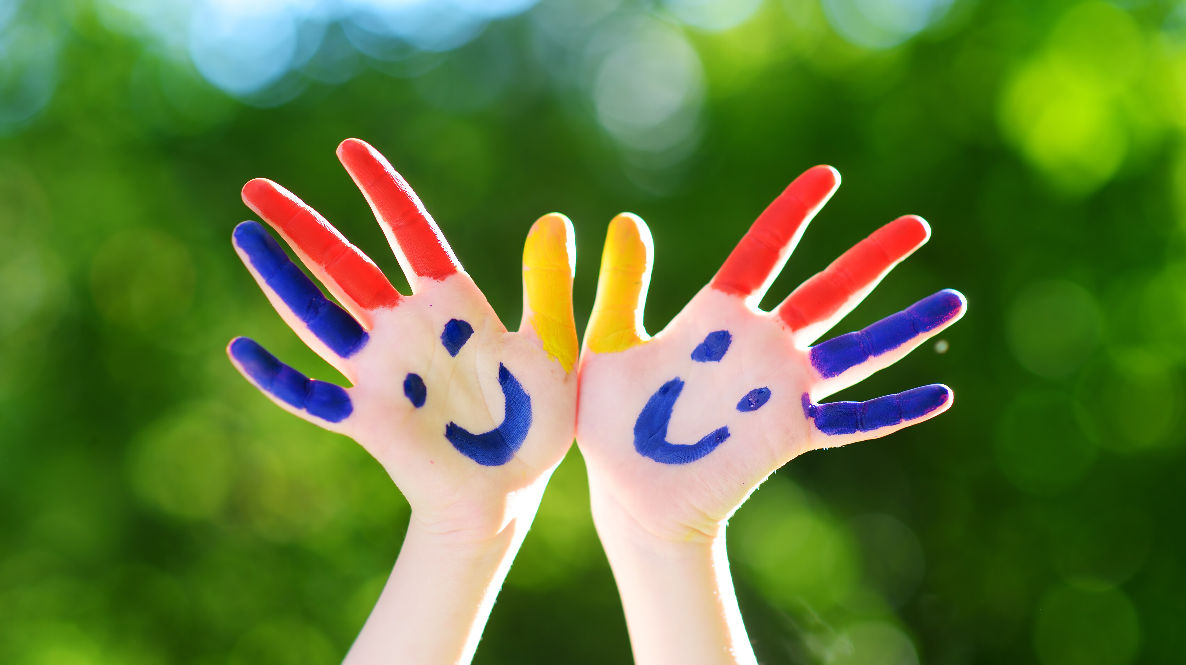 Zwei Hände sind mit bunten Fingerfarben zu grinsenden Gesichtern bemalt.