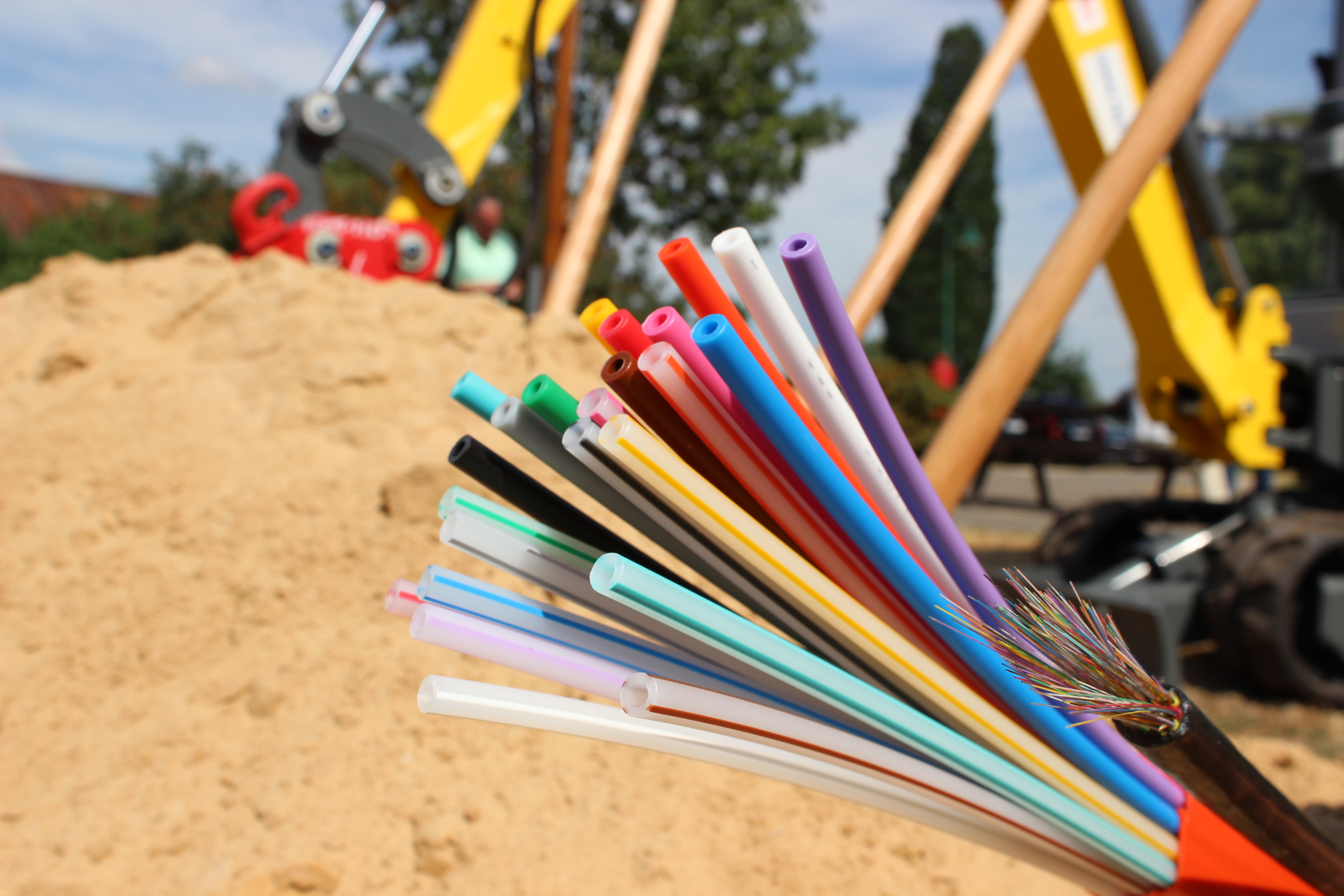Ein Glasfaserkabel vor einer großen Sandhaufen-Baustelle mit einem Bagger.
