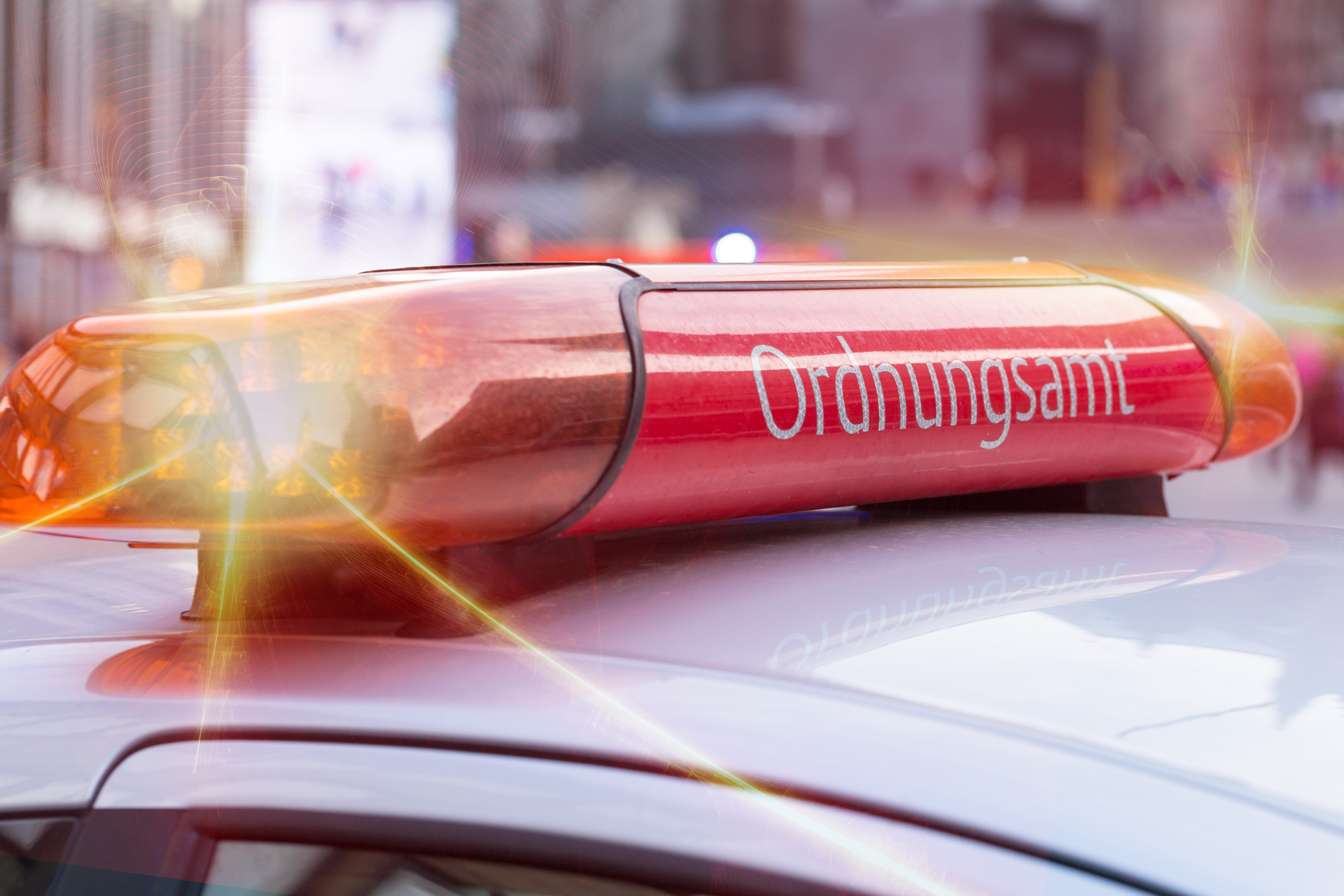 Zwischen zwei blinkenden Warnleuchten steht auf einem Autodach Ordnungsamt.