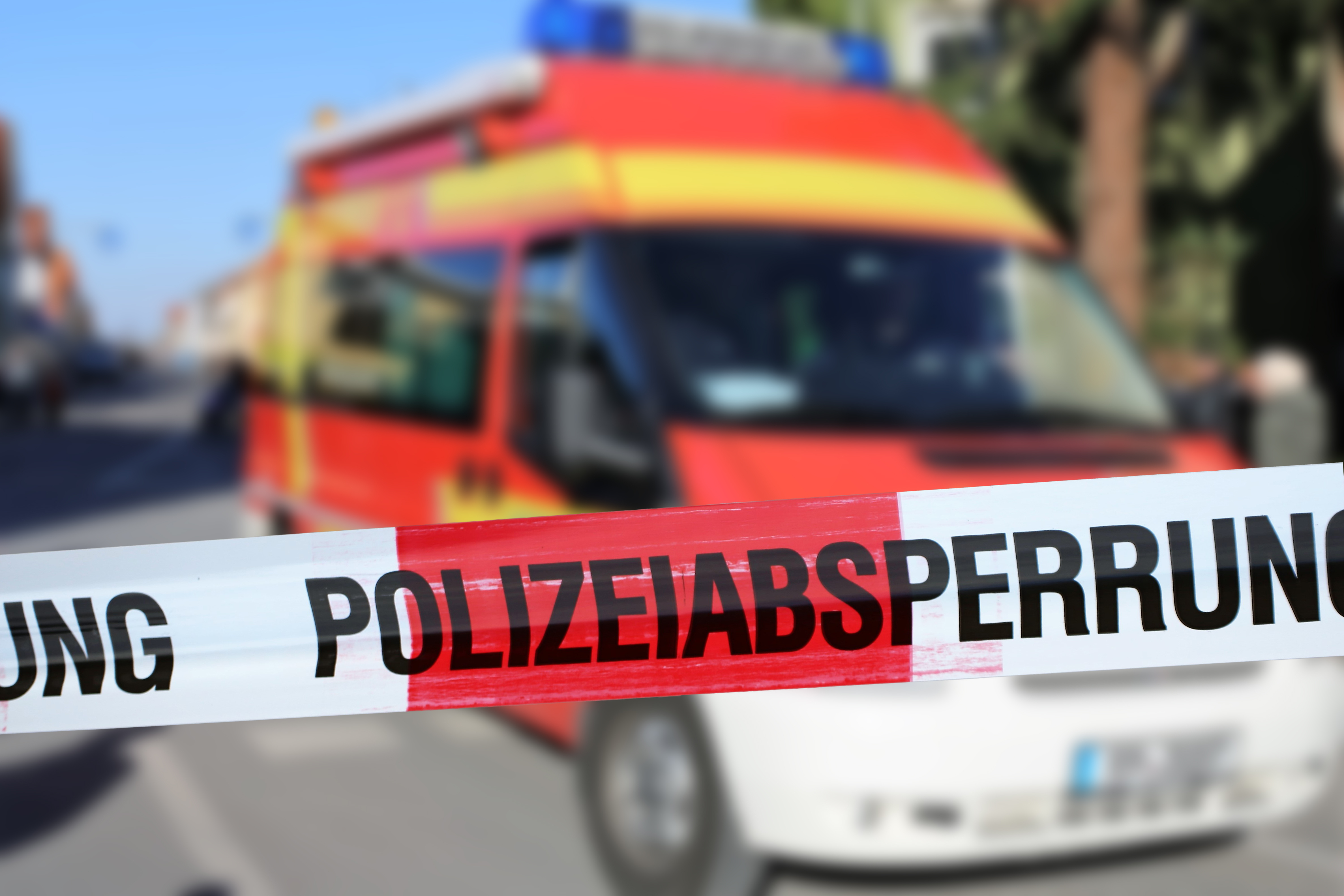 Ein Rettungsfahrzeug steht hinter einem rot-weißem Flatterband mit der Aufschrift Polizeiabsperrung.