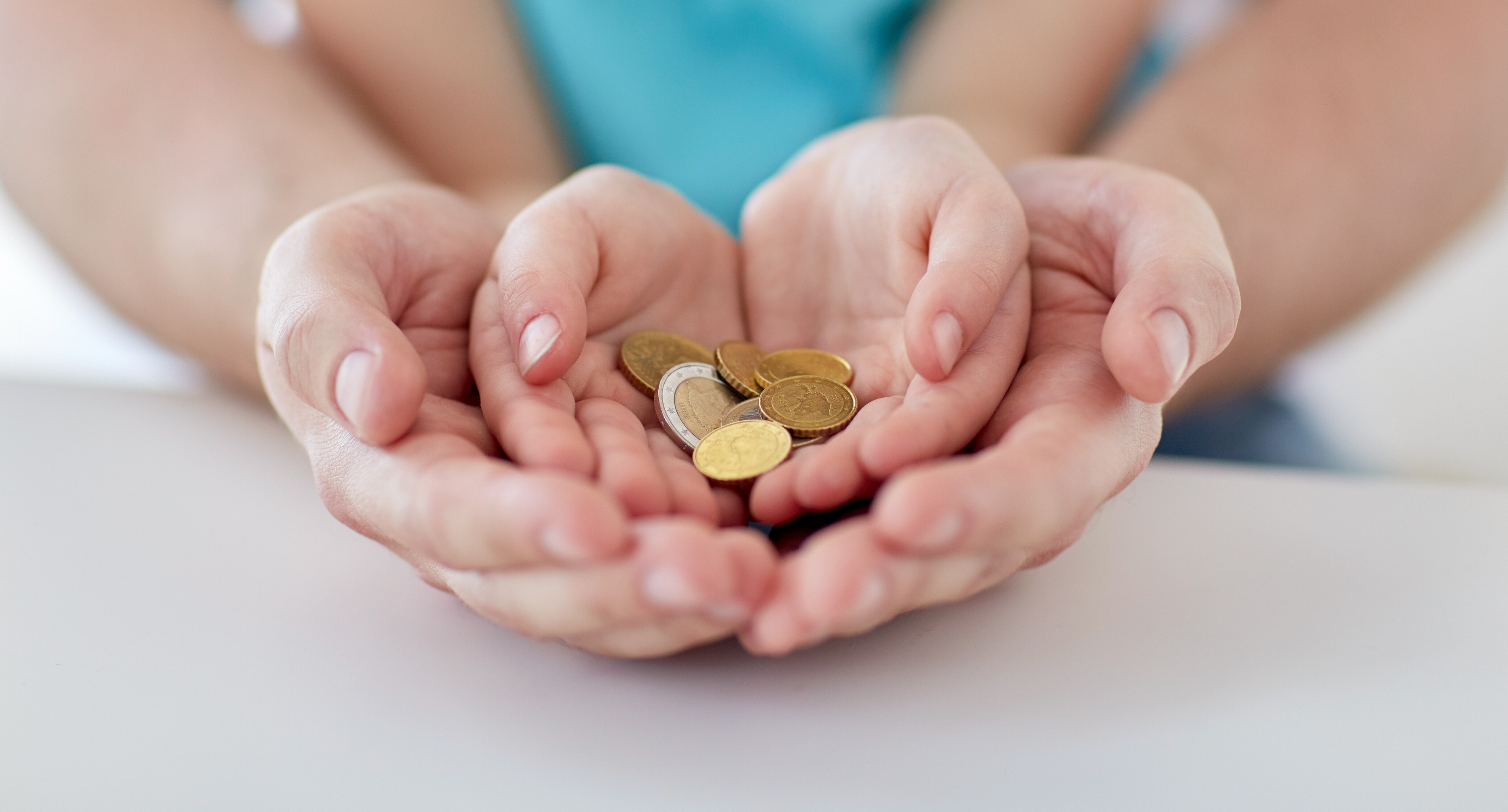 Eine Hand steckt eine Geldmünze in ein kleines gelbes Sparschwein.