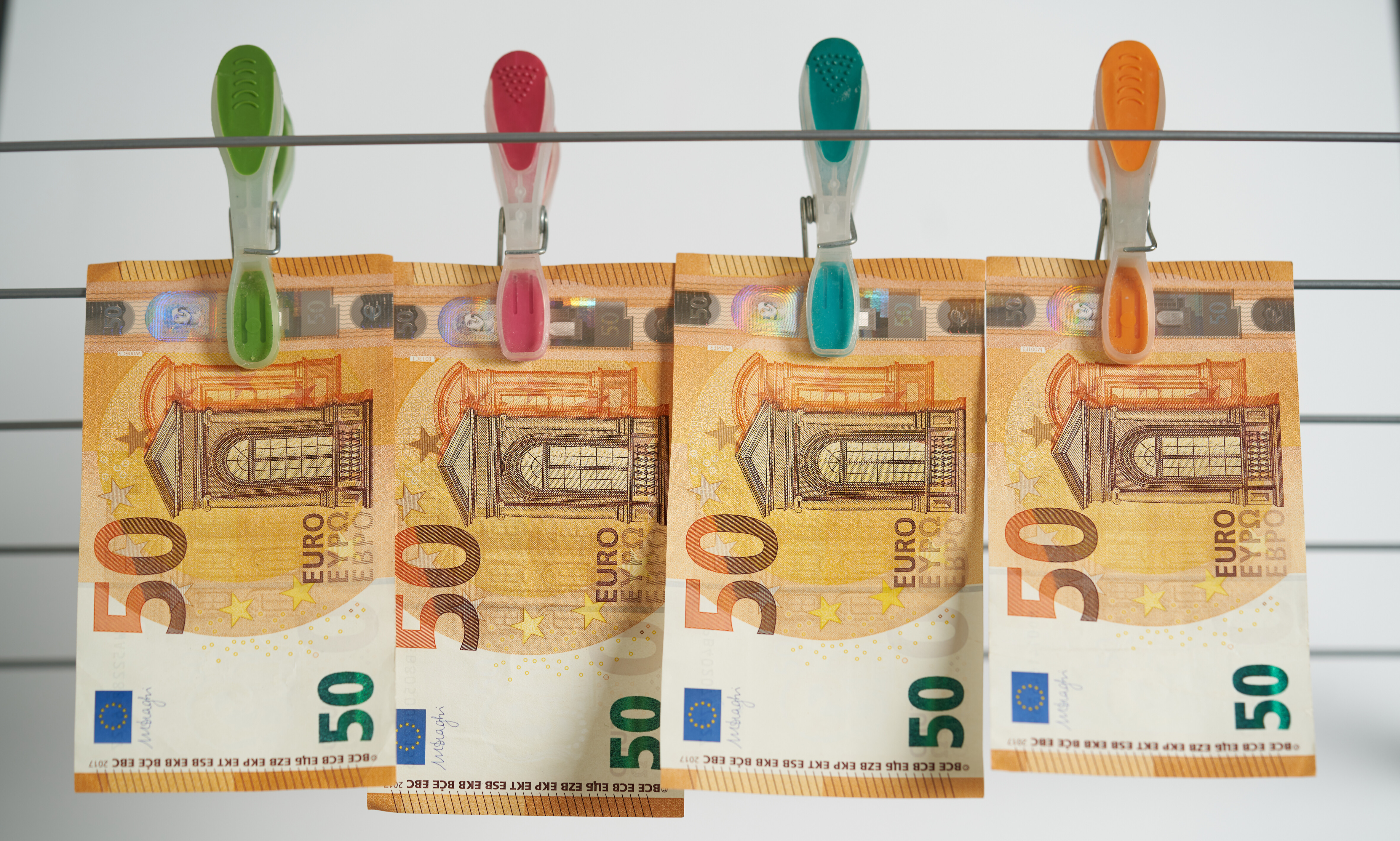 Vier Fünfzigeurobanknoten hängen an Wäscheklammern auf einer Wäscheleine.