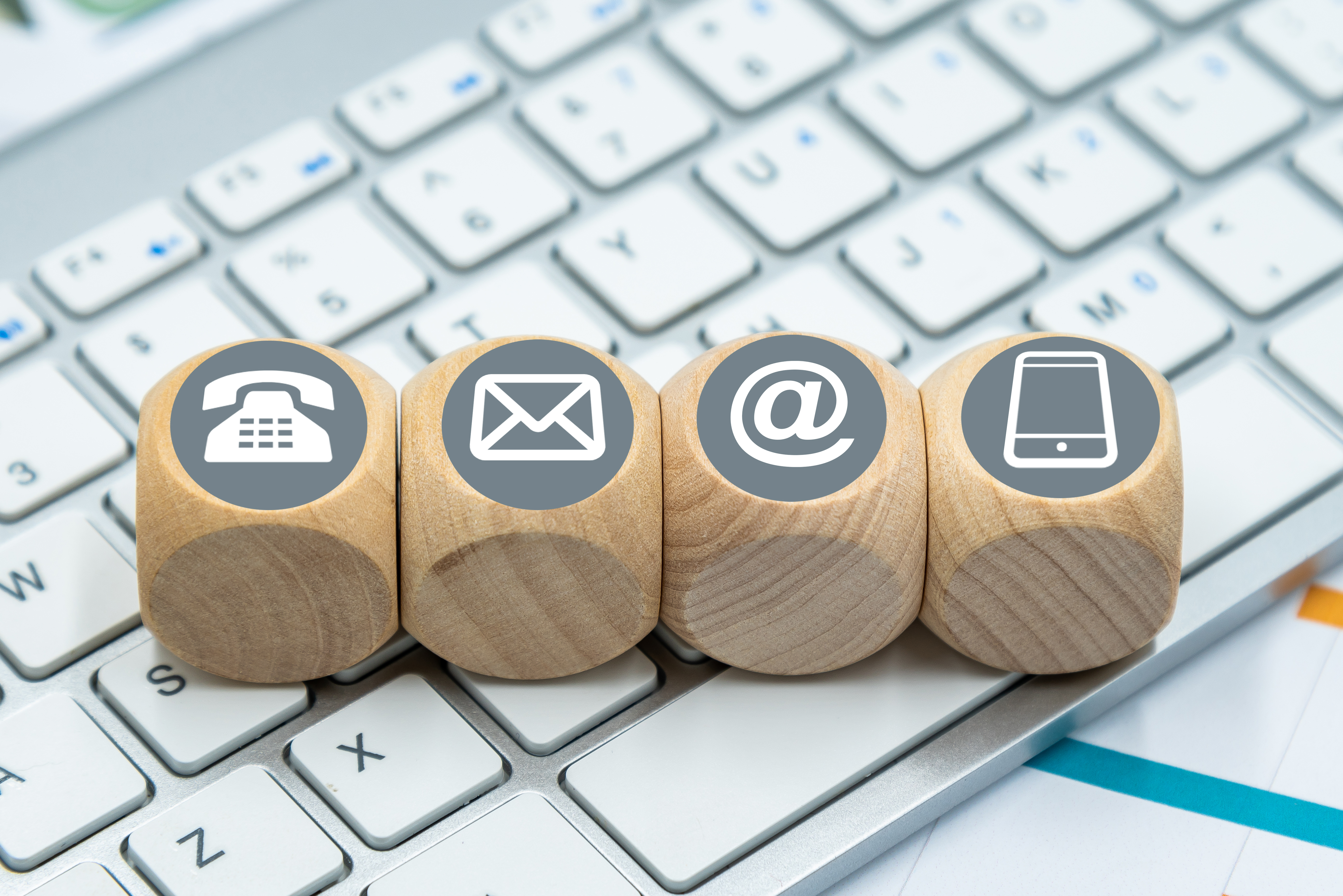 Auf einer Computertastatur finden sich verschiedene Würfel mit den Symbolen der Kommunikation, es gibt ein Telefonsymbol, einen Briefumschlag, ein Internetzeichen und ein Smartphone.