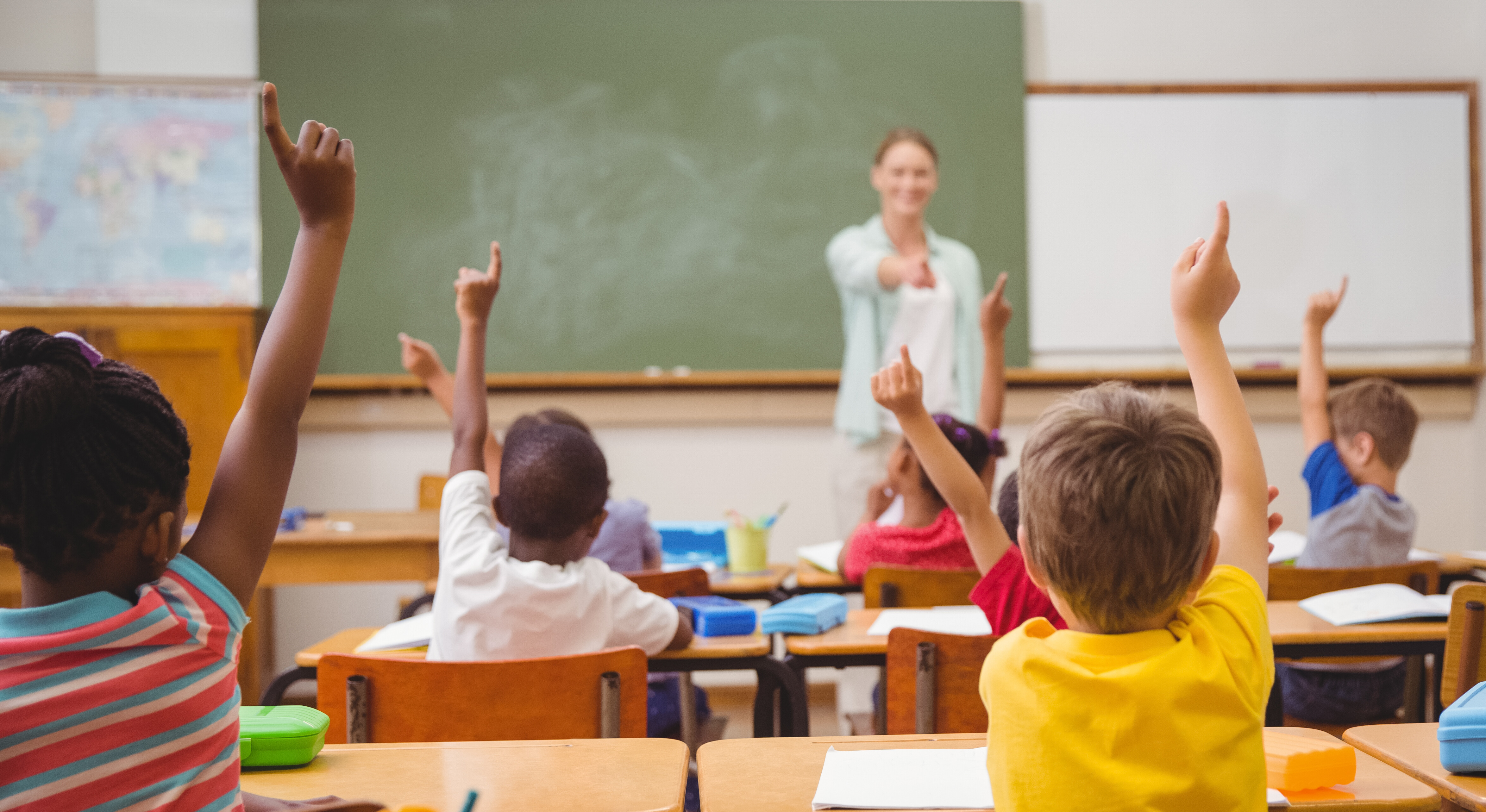 In einem Klassenraum melden sich mehrere Schüler per Handzeichen, um ihrer Lehrerin eine Frage zu beantworten.