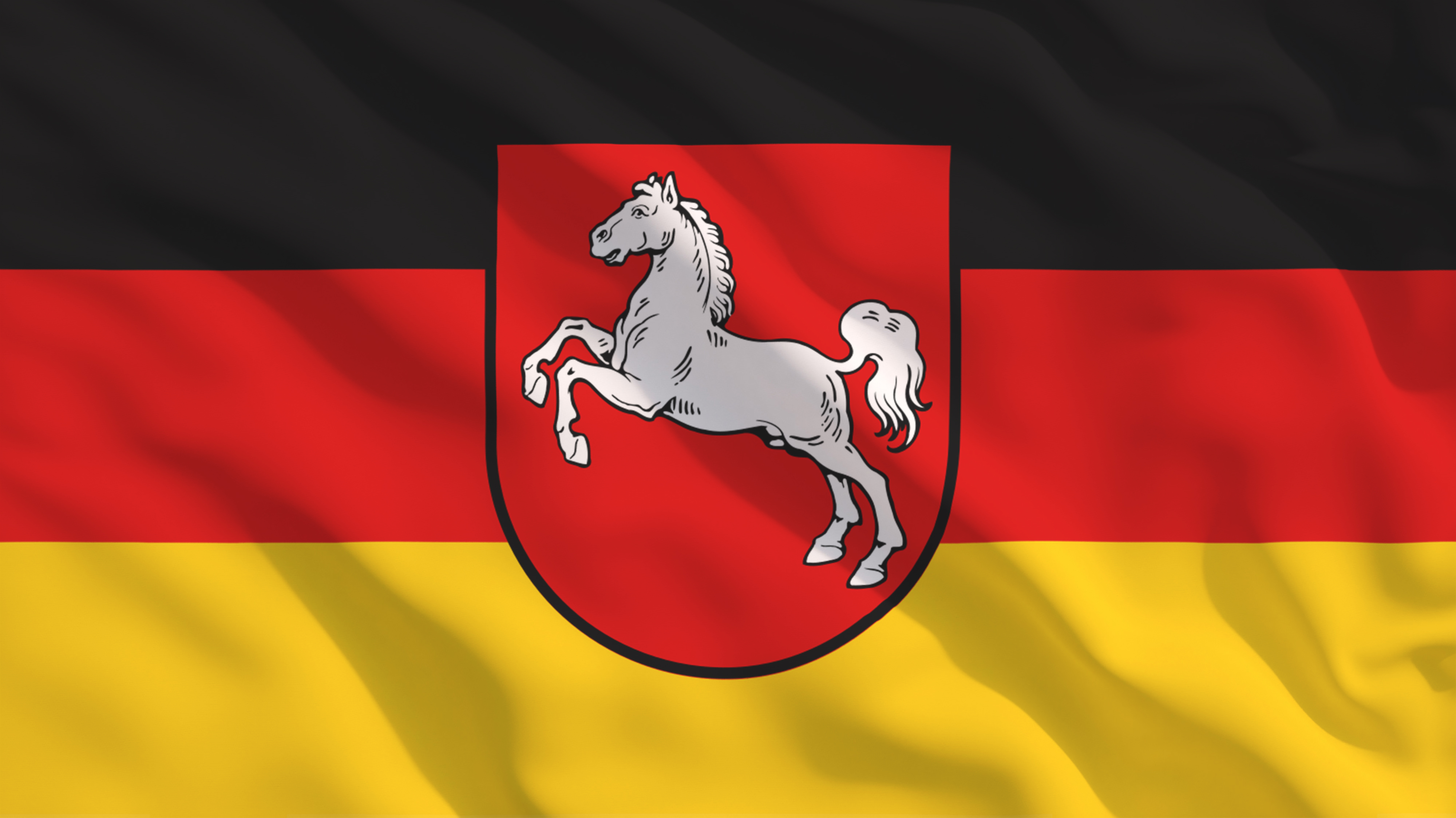 Niedersachsen-Flagge flattert im Wind vor strahlend blauem Himmel.