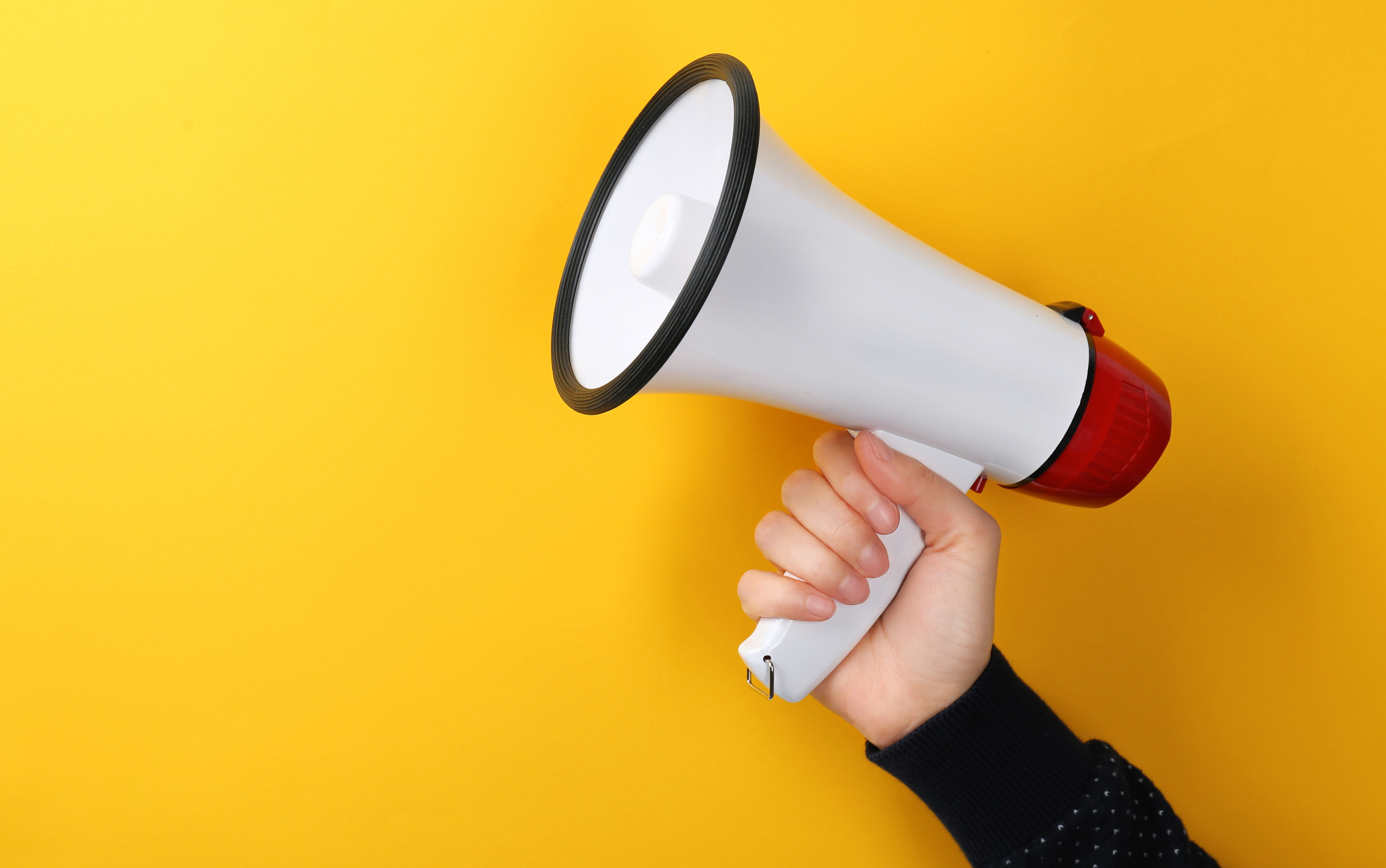 Eine Hand hält ein Megafon vor gelbem Hintergrund.