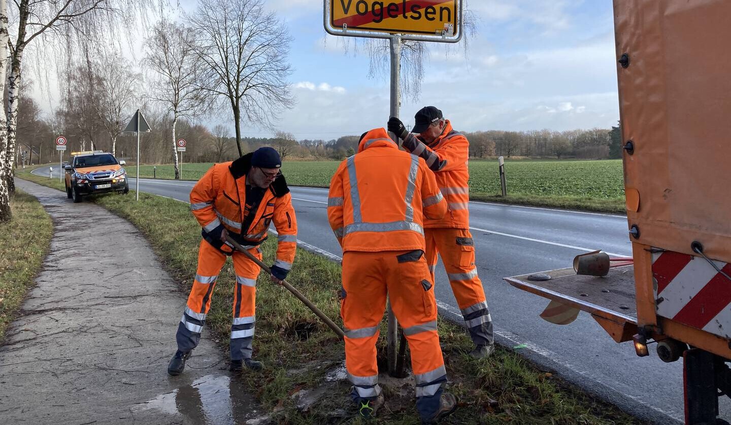 Drei Mitarbeiter des Betriebs Straßenbau und -unterhaltung stellen ein Ortsschild auf.