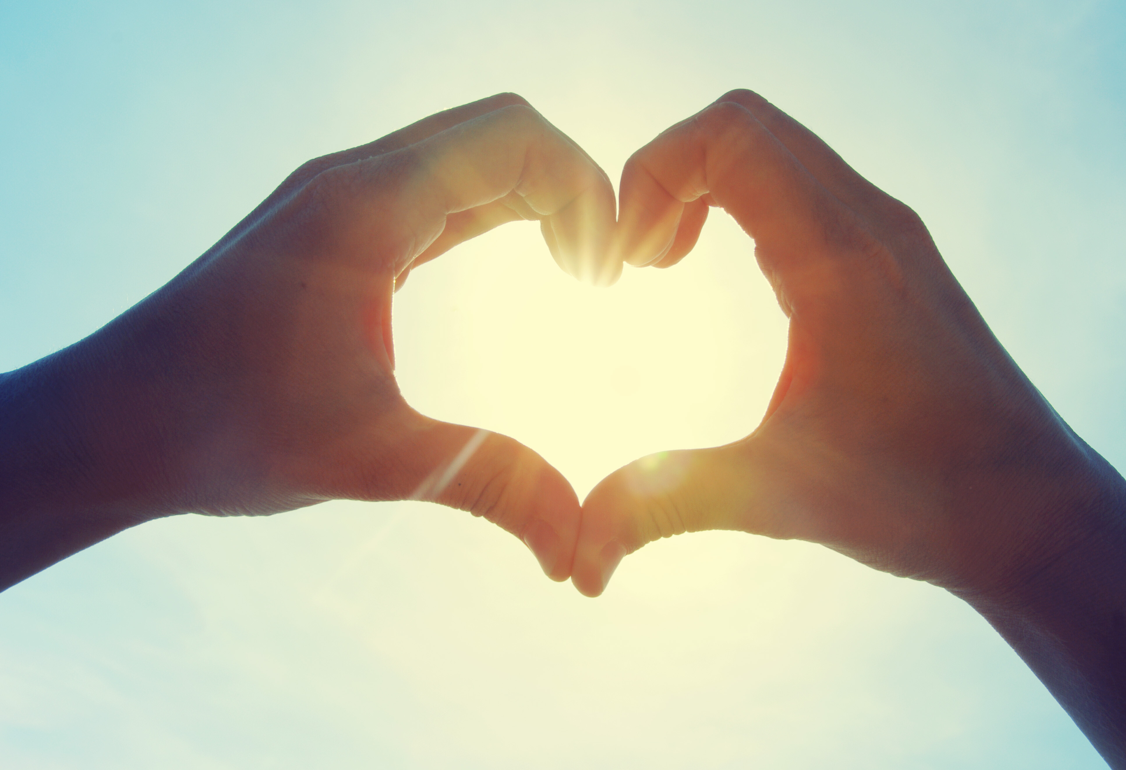 Zwei Hände formen aus den Fingern gemeinsam ein Herz vor der Sonne.