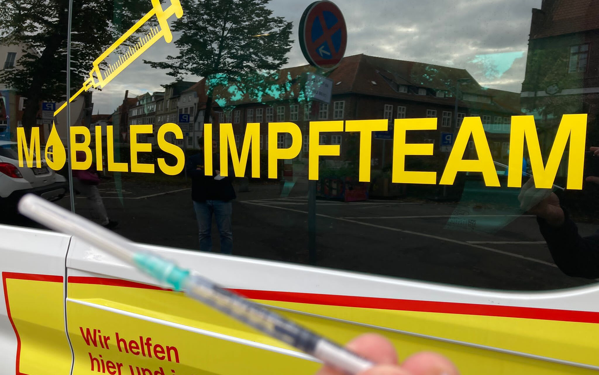 Eine Spritze vor dem Auto mit der Aufschrift Mobiles Impfteam.