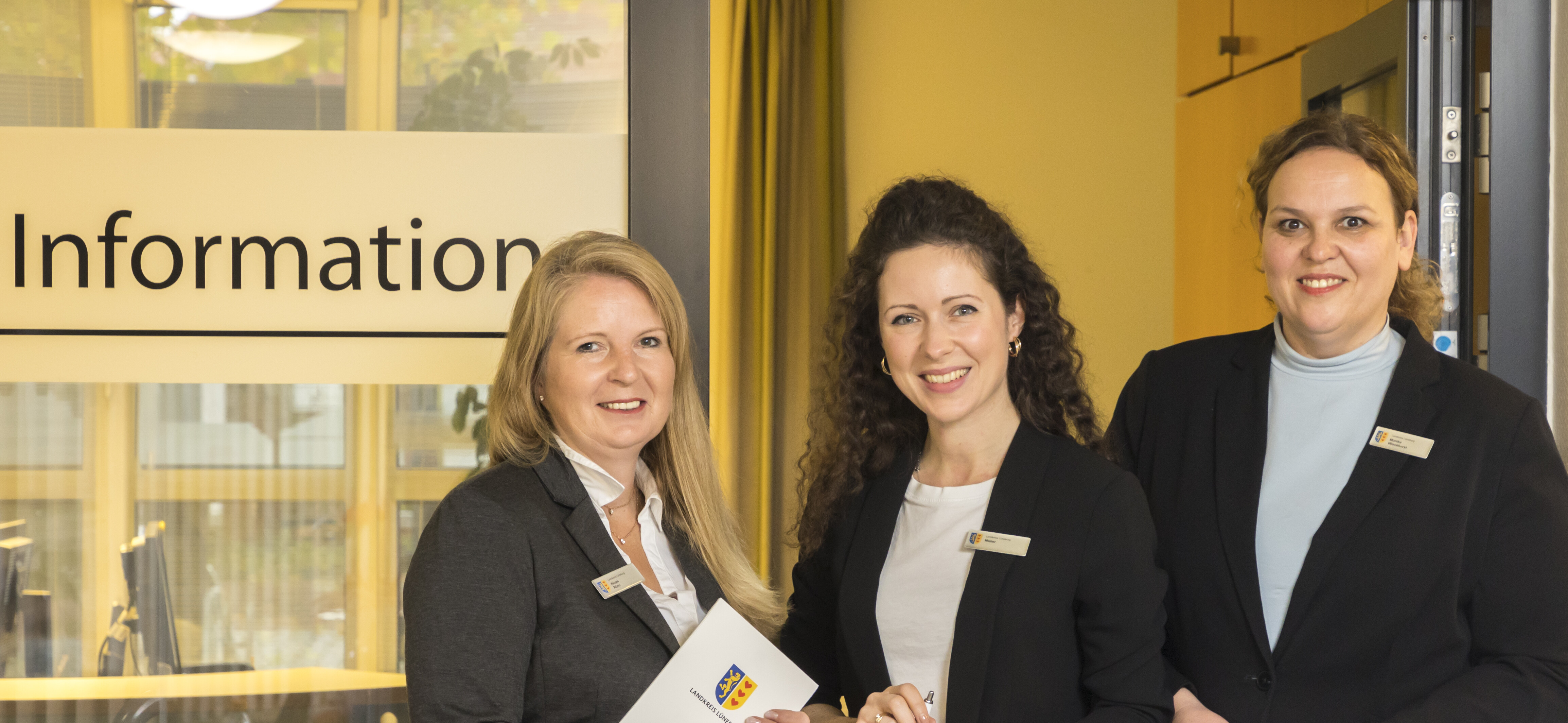 Drei Mitarbeiterinnen der Infothek stehen freundlich vor dem Eingang zu ihrem Büro.