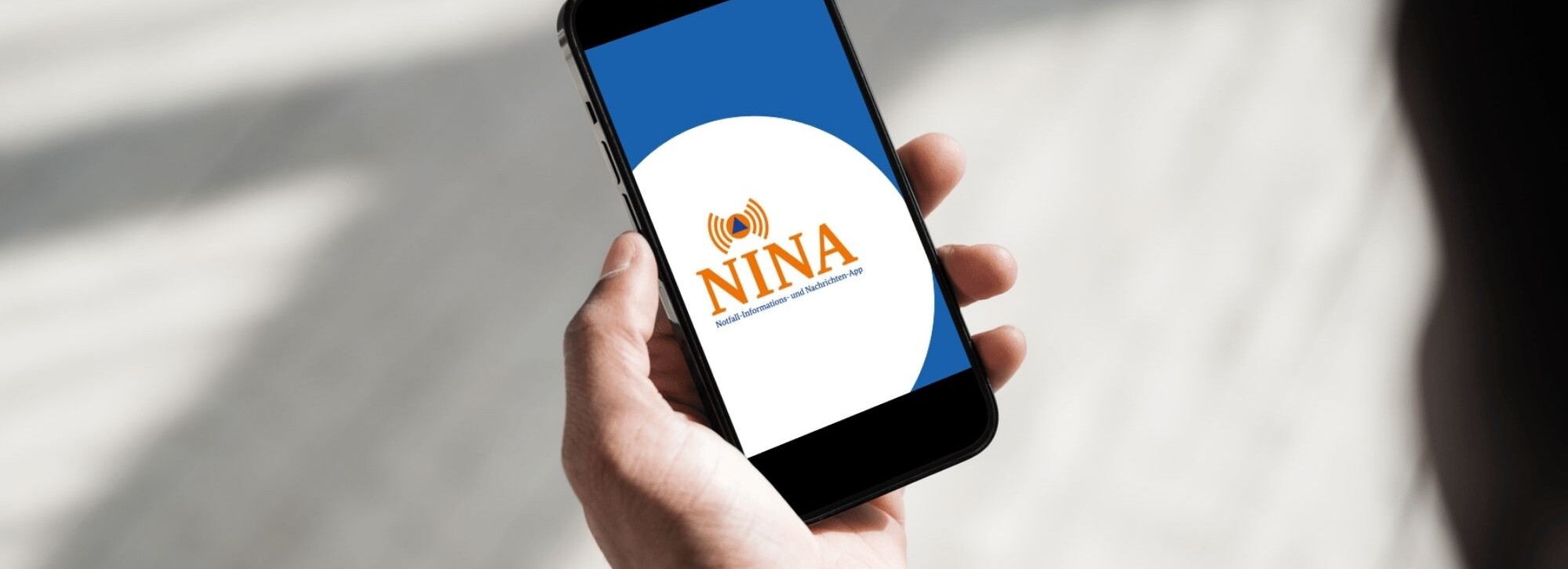 Jemand schaut auf ein Handy, wo das NINA WarnApp Logo erscheint