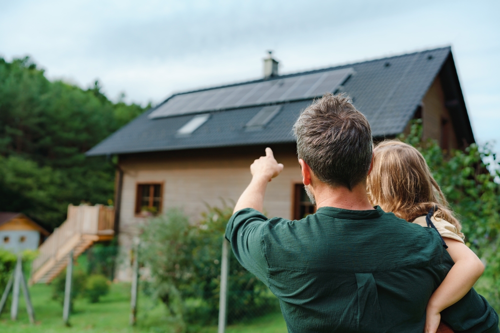 Person steht vor einem Haus mit einer Photovoltaikanlage