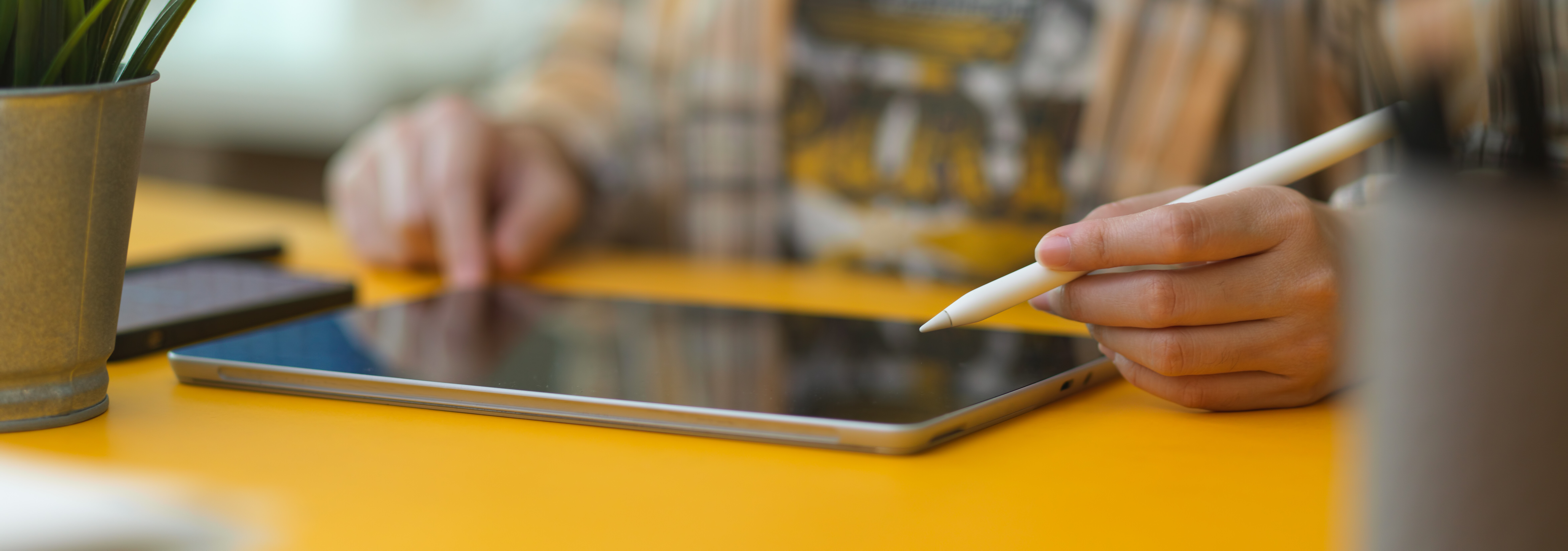 Eine Person sitzt vor einem Tablet. Zu sehen sind lediglich die Hände. 