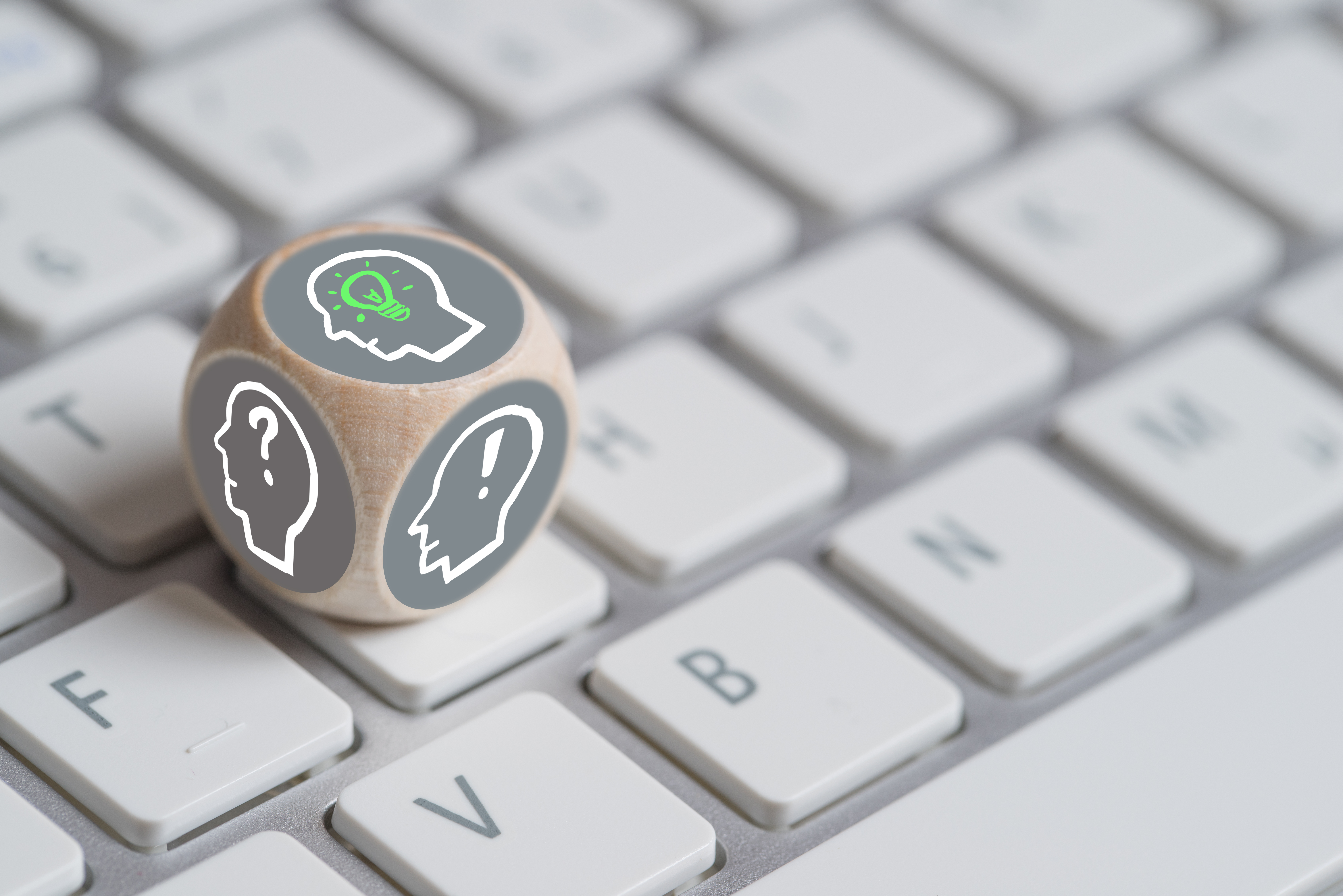 Auf einer Computertastatur liegt ein Würfel mit einem menschlichen Kopf mit Fragezeichen und einem Ausrufezeichen.