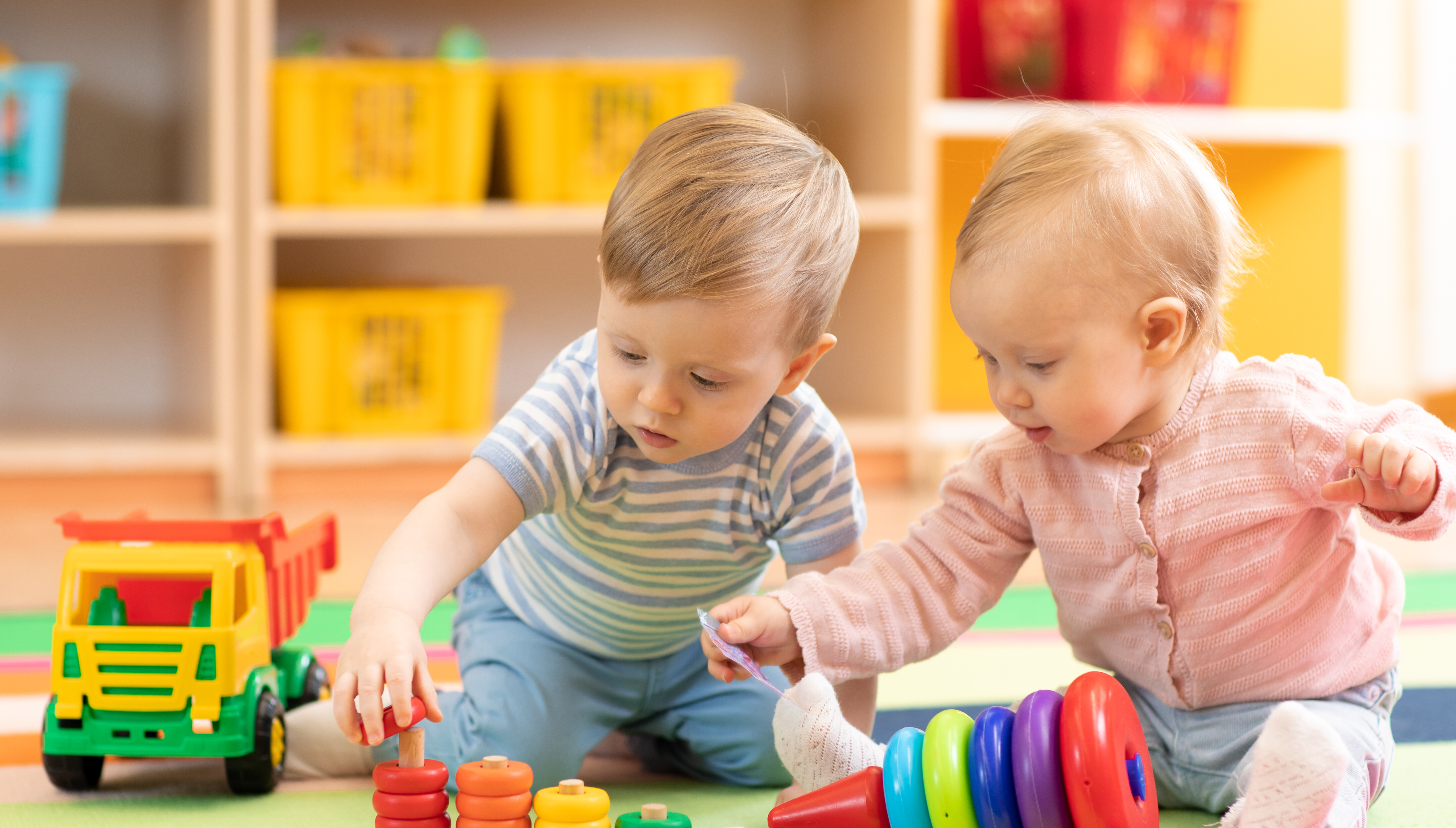 Zwei Kleinkinder spielen zusammen mit buntem Holzspielzeug.