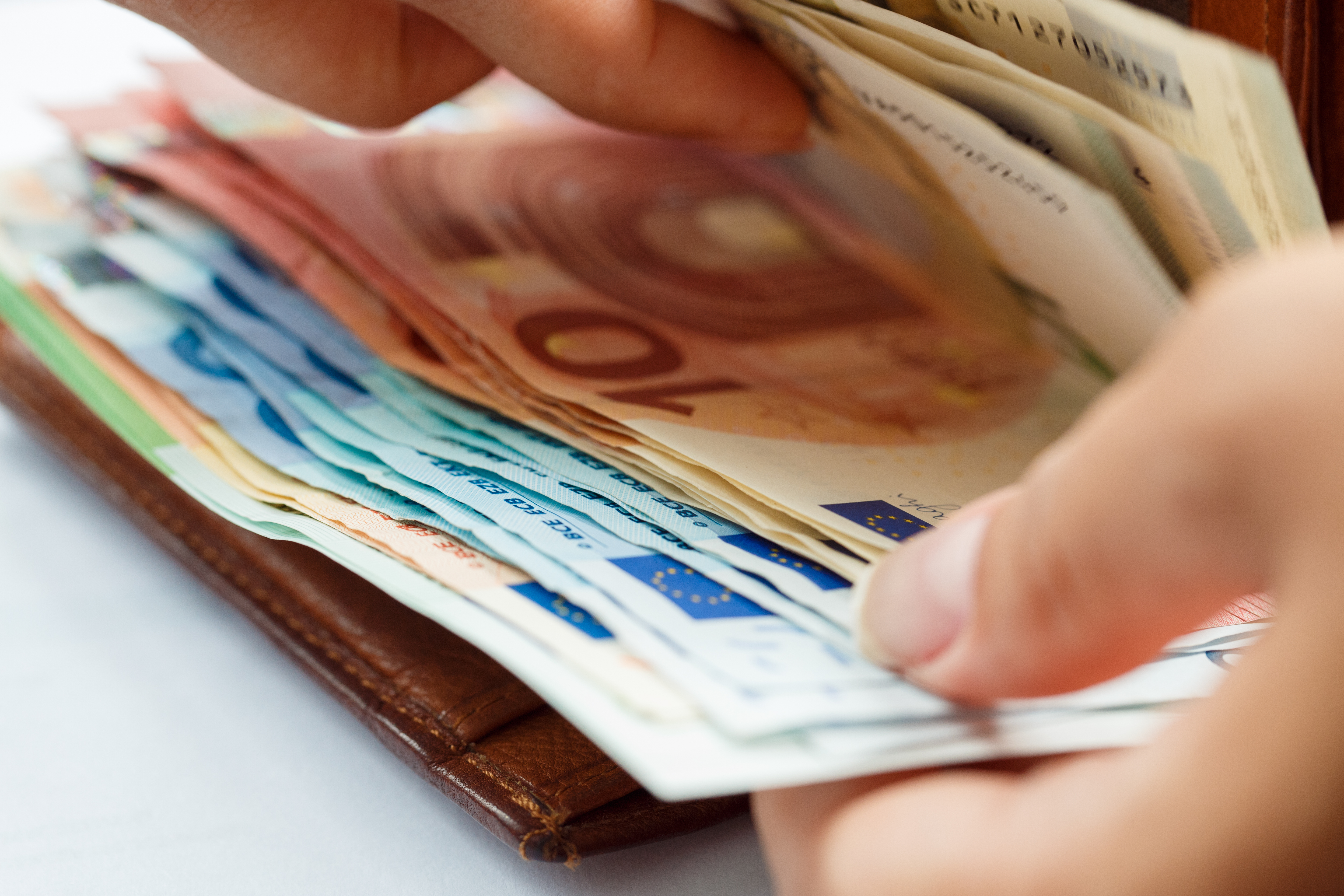 Eine Person zählt viele unterschiedliche Geldscheine vor einer Geldbörse.