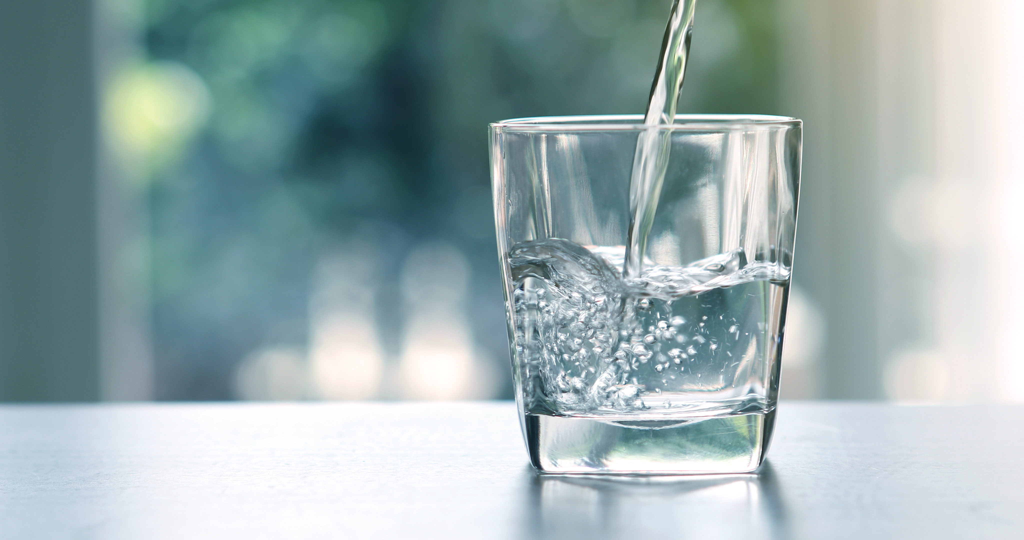 Zwei Hände tragen behutsam ein Glas Trinkwasser.