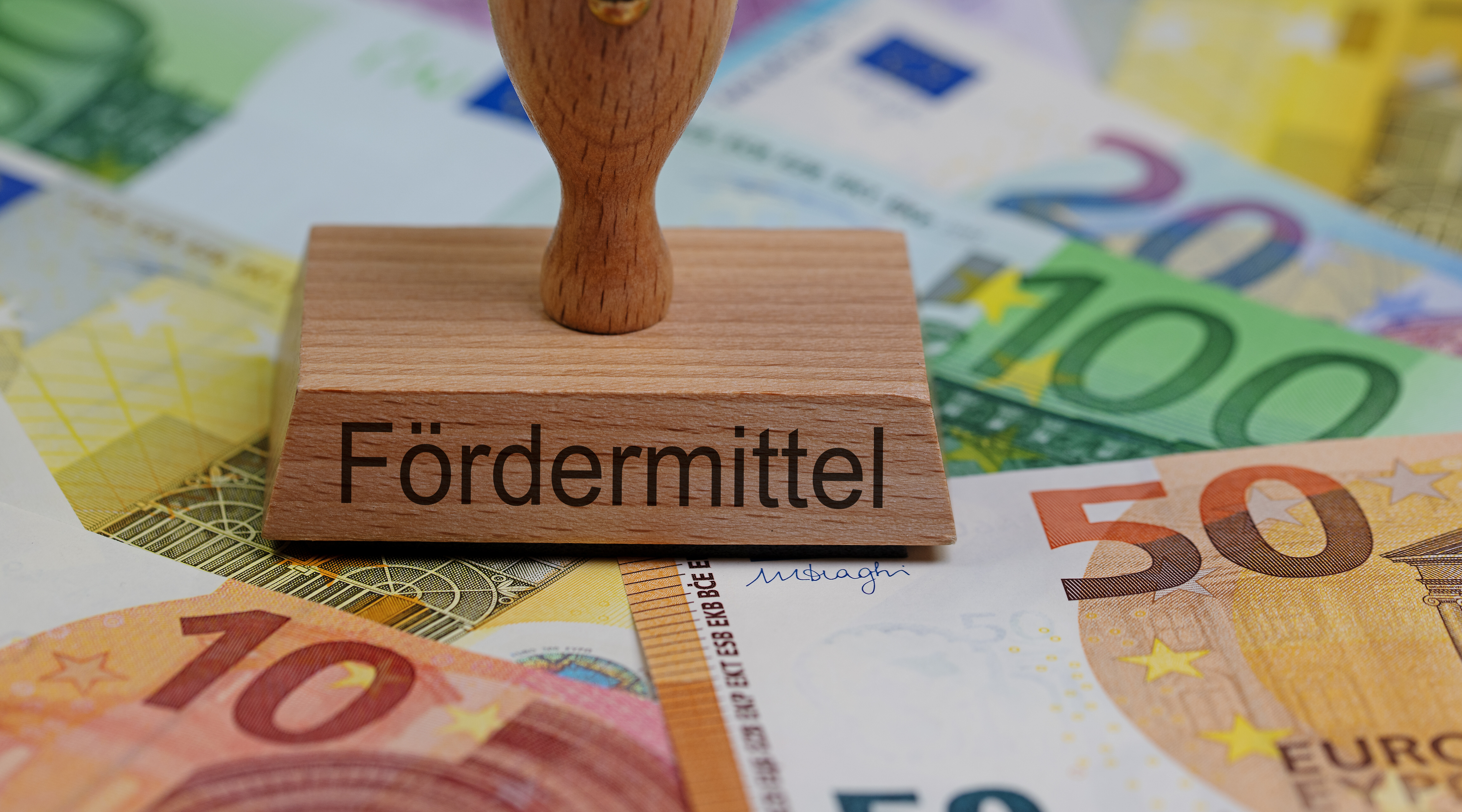 Ein Stempel mit der Aufschrift Fördermittel steht auf verschiedenen Geldscheinen.